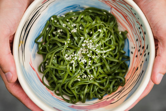 Vista superior de tigela com macarrão verde de algas salpicado com gergelim branco