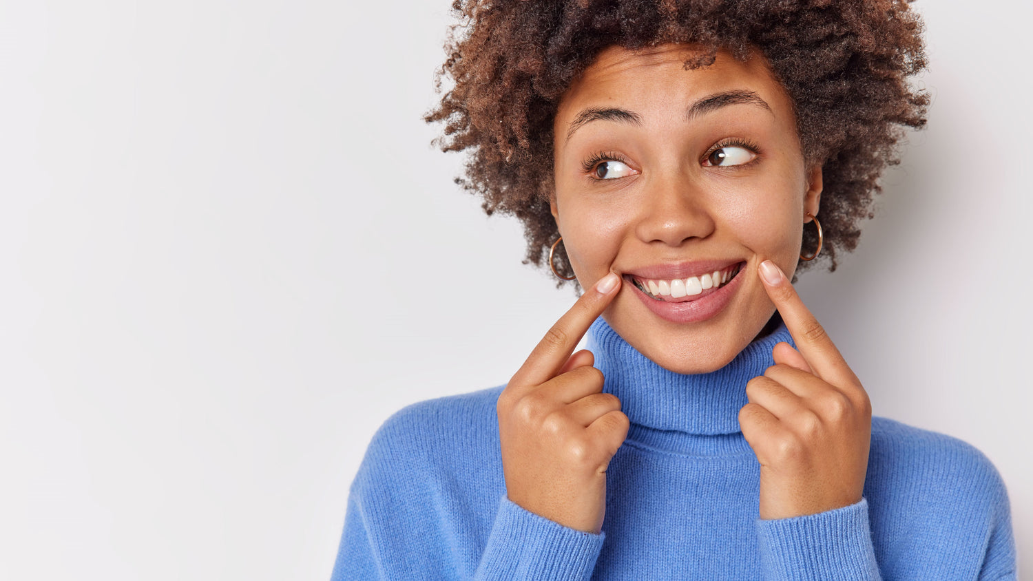 Mulher afro-descendente sorrindo e apoiando os dedos indicadores nos cantos da boca